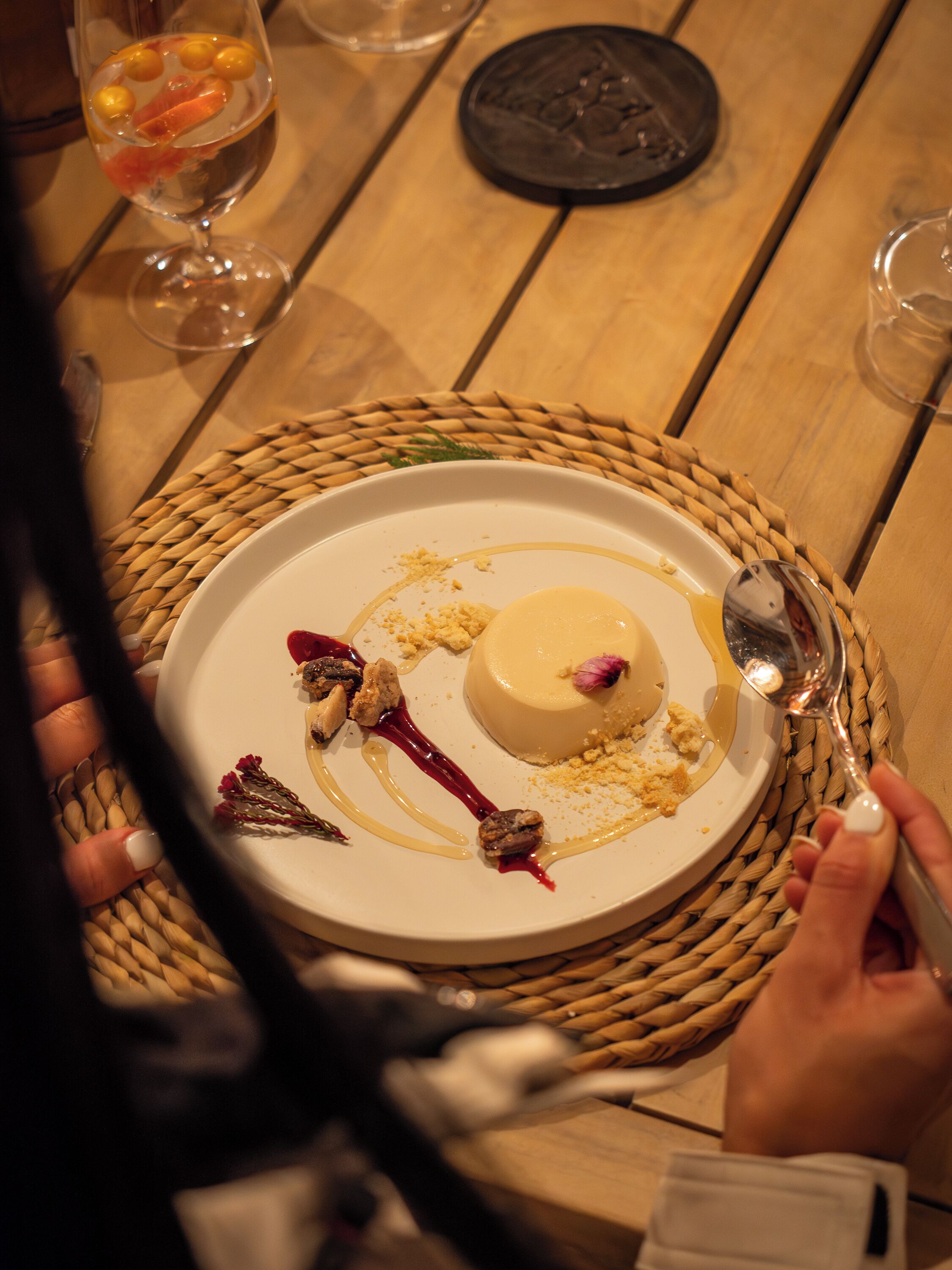 A dessert plate with a scoop of ice cream and garnishes on a woven placemat.