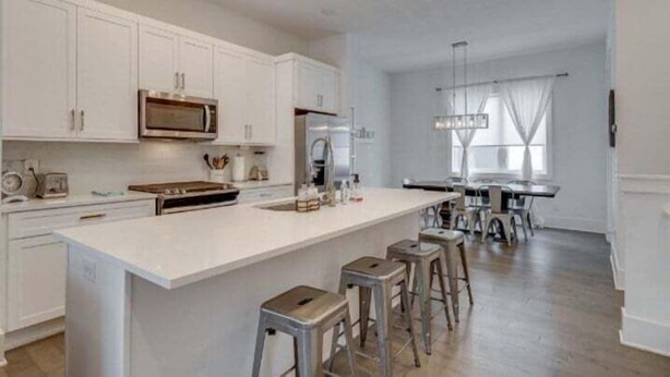 A spacious kitchen with white cabinetry, a central island with stools, and a dining area with a chandelier.
