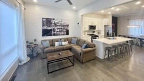 A modern living room with a sectional sofa, a coffee table, and a kitchen area with white cabinets and a central island.