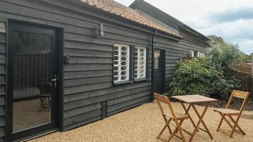 Il s’agit d’un bâtiment en bois à l’extérieur noir, doté d’une porte coulissante en verre et d’un petit espace patio avec deux chaises et une table en bois.