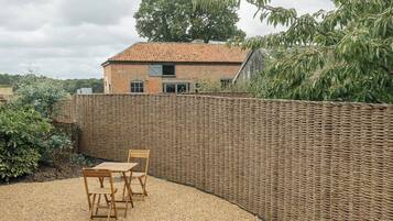 A patio with a wicker wall, a brick house in the background, and a gravel ground.