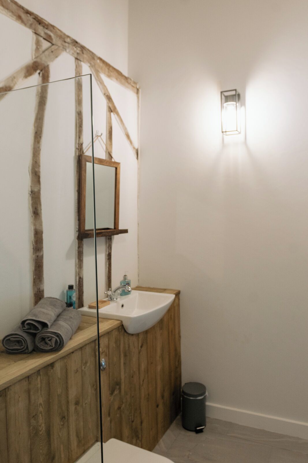 A bathroom with a wooden vanity, a white sink, a mirror, and a wall-mounted light fixture.