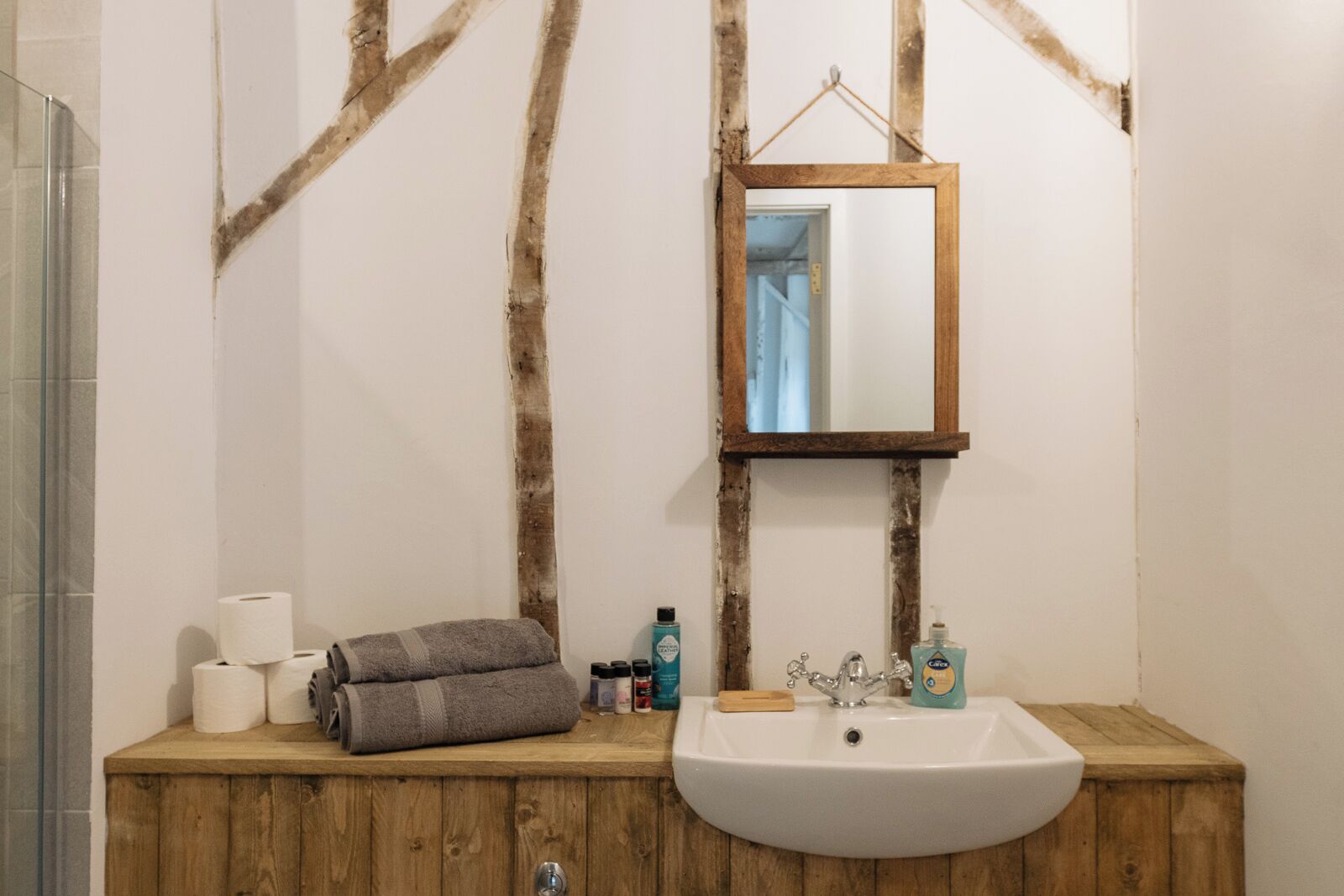 Une salle de bain avec un meuble-lavabo en bois, un lavabo blanc, un miroir et des articles de toilette.