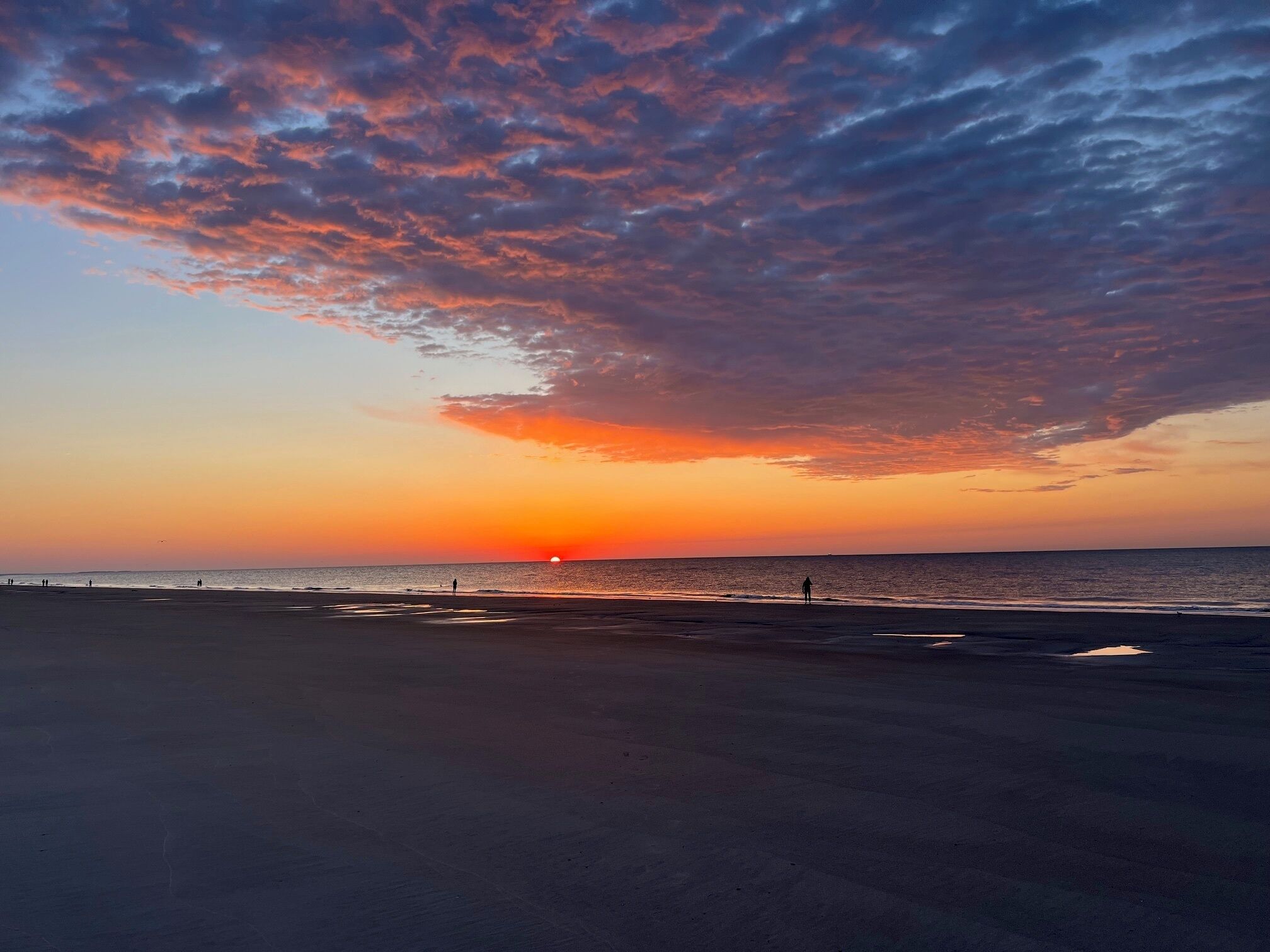 En strand med solnedgang, en person der går, og havet.
