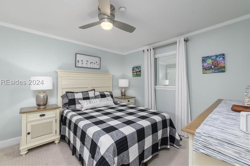 Une chambre à coucher avec une couvre-lit à carreaux, un ventilateur de plafond, des lampes de chevet, une table de chevet et une fenêtre avec des rideaux.