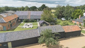 A courtyard with multiple buildings, some with tiled roofs and others with brick walls. There are outdoor seating areas and a grassy lawn. - 4 Henham Barns, Henham Park nr Southwold, NR34 8AQ, Carefully restored Character filled barn (Beccles)
