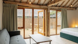 A room with a bed, a sofa, a table, and large windows. - 4 Henham Barns, Henham Park nr Southwold, NR34 8AQ, Carefully restored Character filled barn (Beccles)