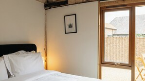 Une chambre à coucher avec un lit, une plante en pot et une fenêtre donnant sur un immeuble et une clôture.