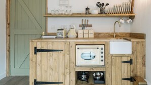 Une cuisine compacte équipée d’un four encastré, d’un évier et d’une machine à café. Des étagères au-dessus du plan de travail servent à ranger la vaisselle et une bouilloire.