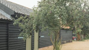 Un bâtiment à l’extérieur sombre, avec une porte verte, entouré de gravier et d’un arbre.