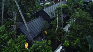 A multi-story building with a dark roof, surrounded by dense greenery.