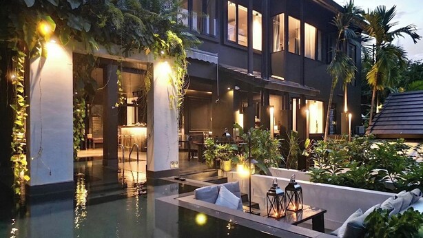 A modern hotel with a pool area, outdoor seating, and lush greenery.