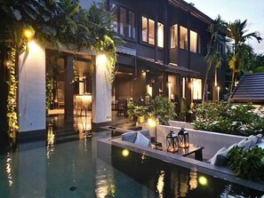 Un hotel moderno con zona de piscina, mobiliario exterior y abundante vegetación.