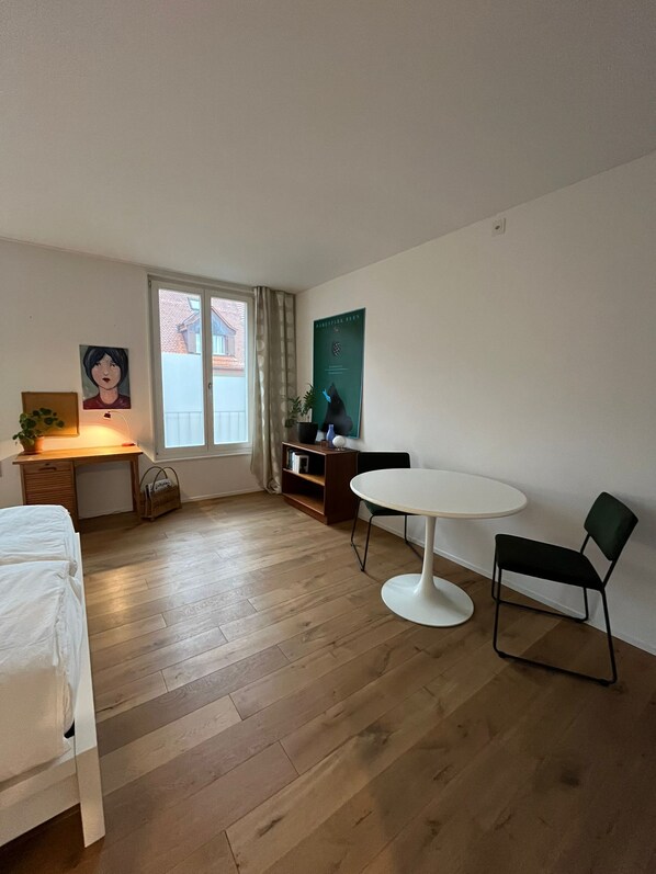 A room with a bed, a desk, a chair, a small table, and a window with curtains.