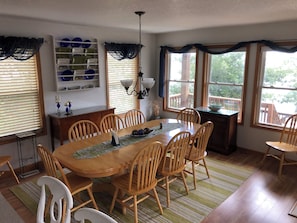 Un comedor con una mesa y sillas de madera, una araña y un ventanal con vista a árboles.