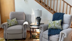 A living room with two armchairs, a small table with a lamp, a striped rug, and a staircase with a painting above it. - NEW LISTING: Breathtaking Waterfront Views w/ Private Dock  (Kill Devil Hills)