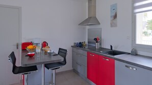 Una cocina moderna con zona de comedor, que cuenta con un lavamanos de acero inoxidable, armarios rojos y una ventana con vistas.