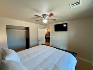 Une chambre à coucher comprenant un lit, un ventilateur de plafond, un téléviseur et une porte donnant sur la cuisine.