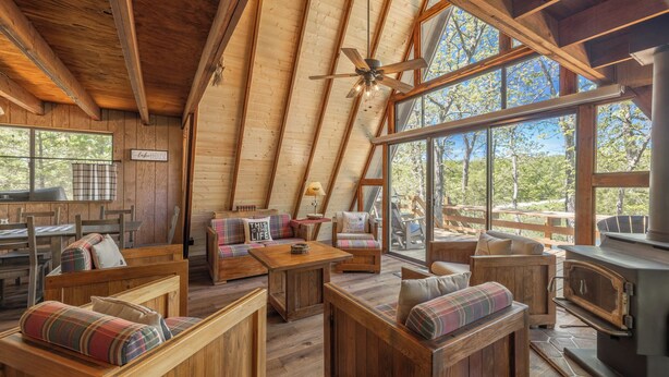 A cozy log cabin interior with wooden furniture, a fireplace, and large windows offering a view of the outdoors. - Rustic Fox by Innsbrook Vacations! (Innsbrook)