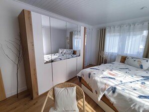 A bedroom with a bed, a chair, a mirror, and a window with curtains. - Family-friendly apartment to feel good with flair and a large balcony  (Langenzenn)
