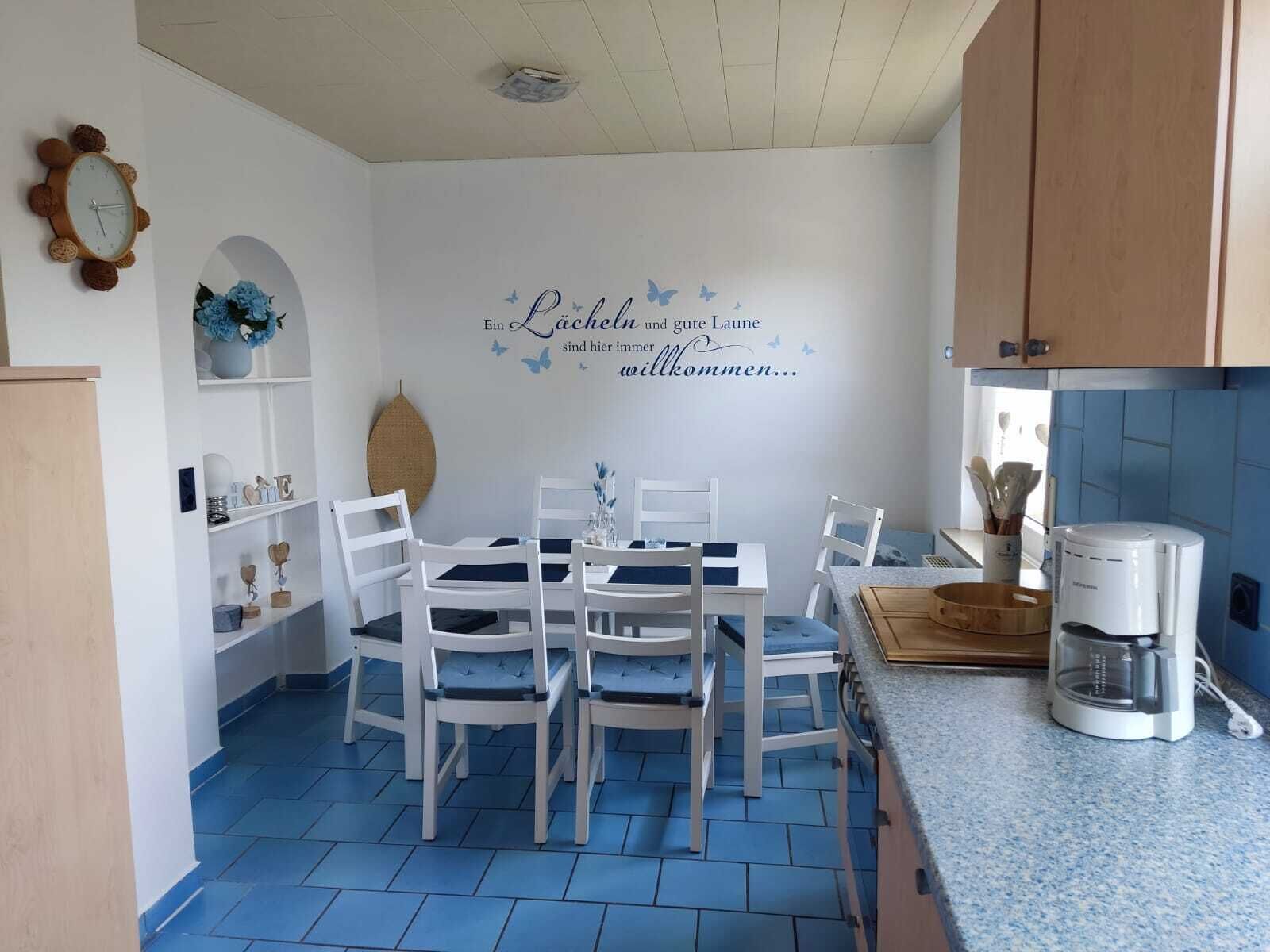A dining area with a white table and chairs, a coffee machine, and a wall with a welcome message.