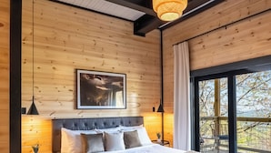 Een slaapkamer met een groot bed, een bankje, een hanglamp en een raam met uitzicht.