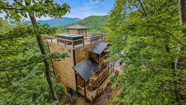 Een houten hut met een jacuzzi, buitenmeubels en uitzicht op bos en bergen.