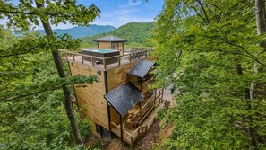 A wooden cabin with a hot tub, outdoor seating, and a view of the forest and mountains. - Skyscraper Chalet | Rooftop Pool | Ober Mountain Views (Gatlinburg)
