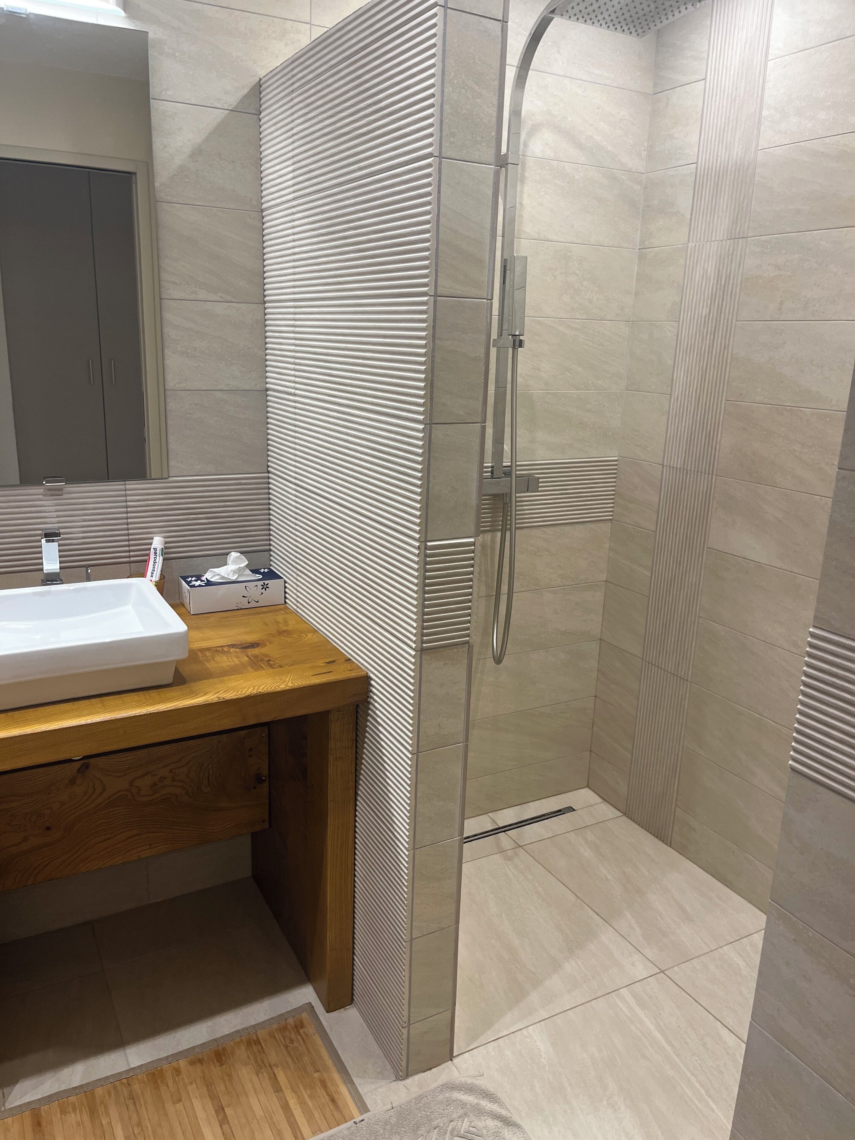 A modern bathroom with a shower, a wooden vanity, and a white sink.