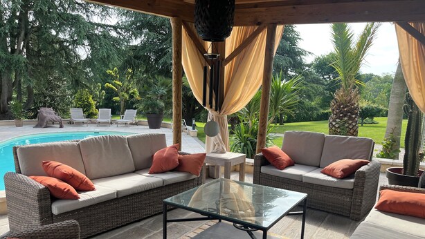 Un espacio de patio al aire libre con mobiliario de mimbre, una mesa de centro de vidrio y una piscina al fondo.