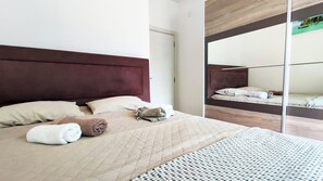 Relax in a spacious room with a large bed and a stylish headboard, complemented by a large mirror and a minimalist design.