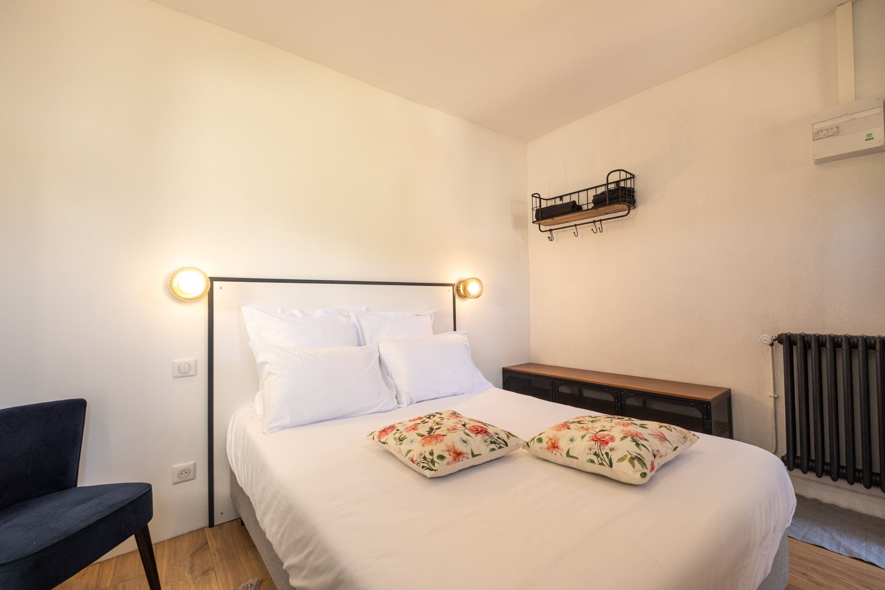 Un dormitorio con cama, mesita de noche, silla y estante en la pared.