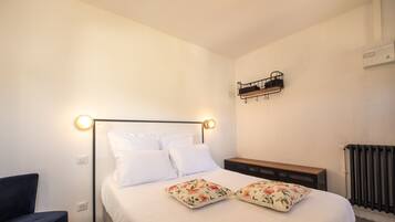 Un dormitorio con cama, mesita de noche, silla y estante en la pared.