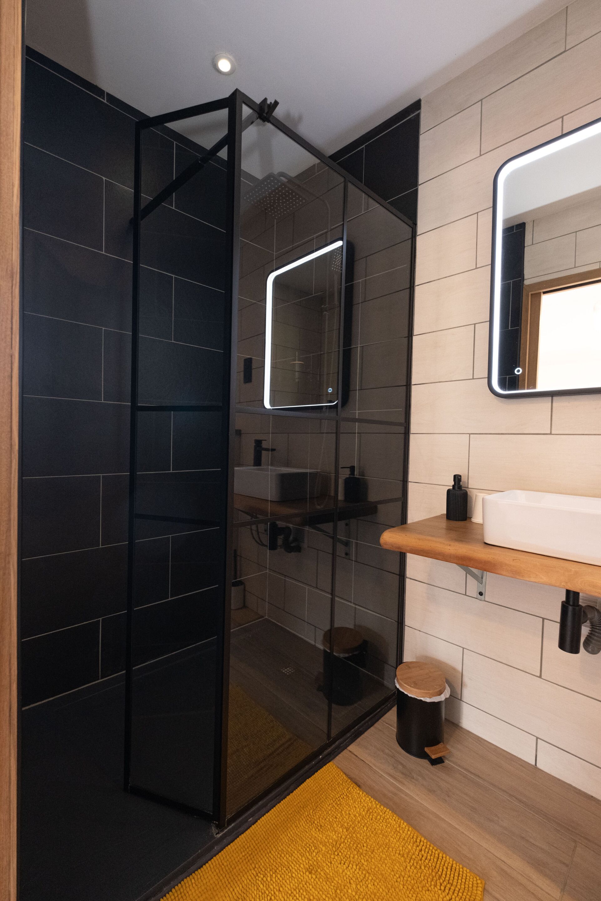 A modern bathroom with a glass-enclosed shower, a wooden vanity, and a mirror above the sink.