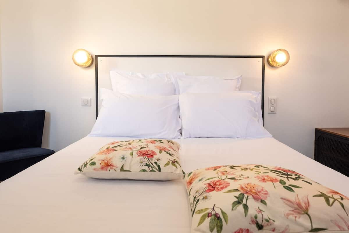 Een net opgemaakt bed met witte lakens en kussens met bloemenmotief, een zwart hoofdbord en wandlampen.