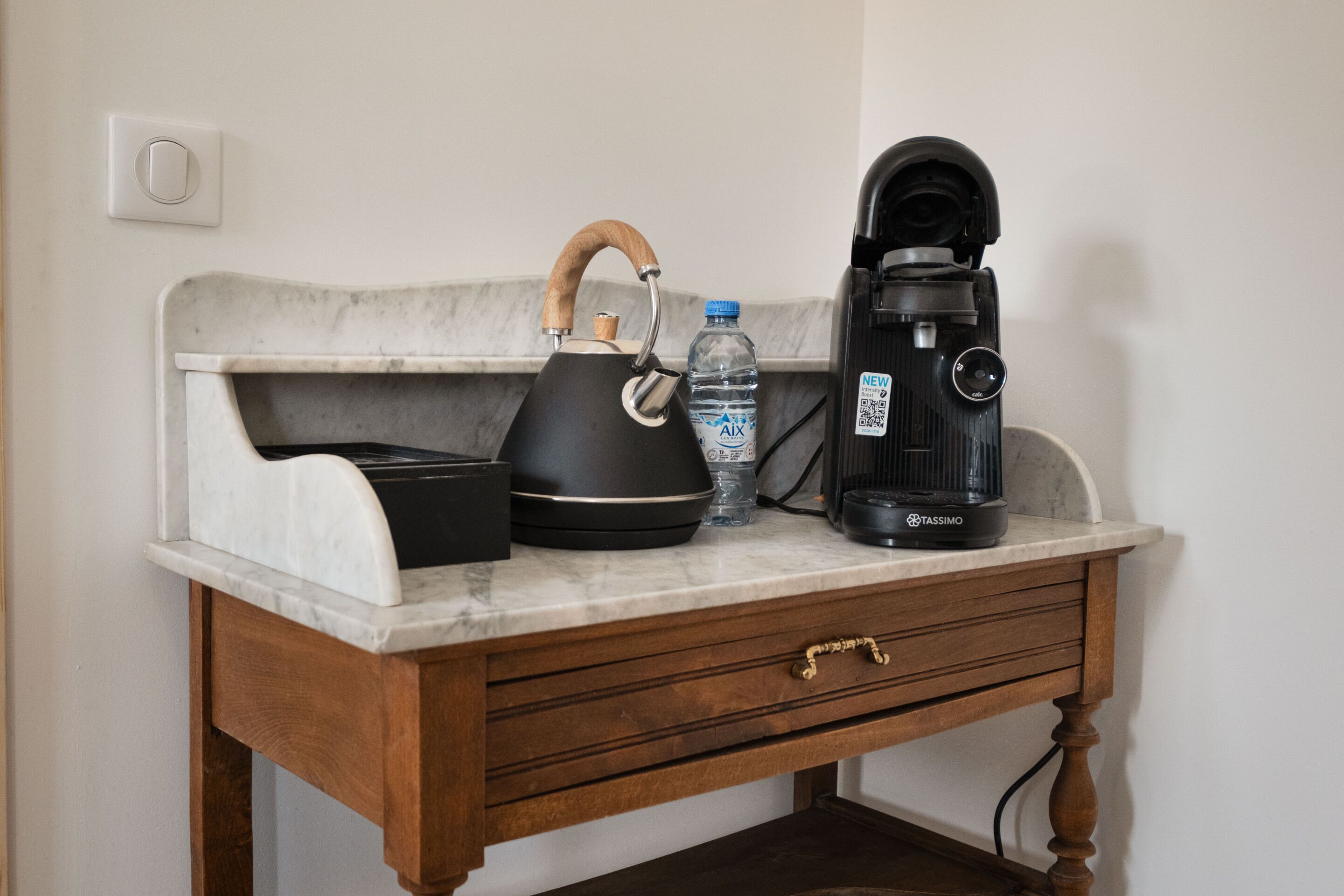 A kitchen counter with a kettle, a water bottle, and a coffee maker.