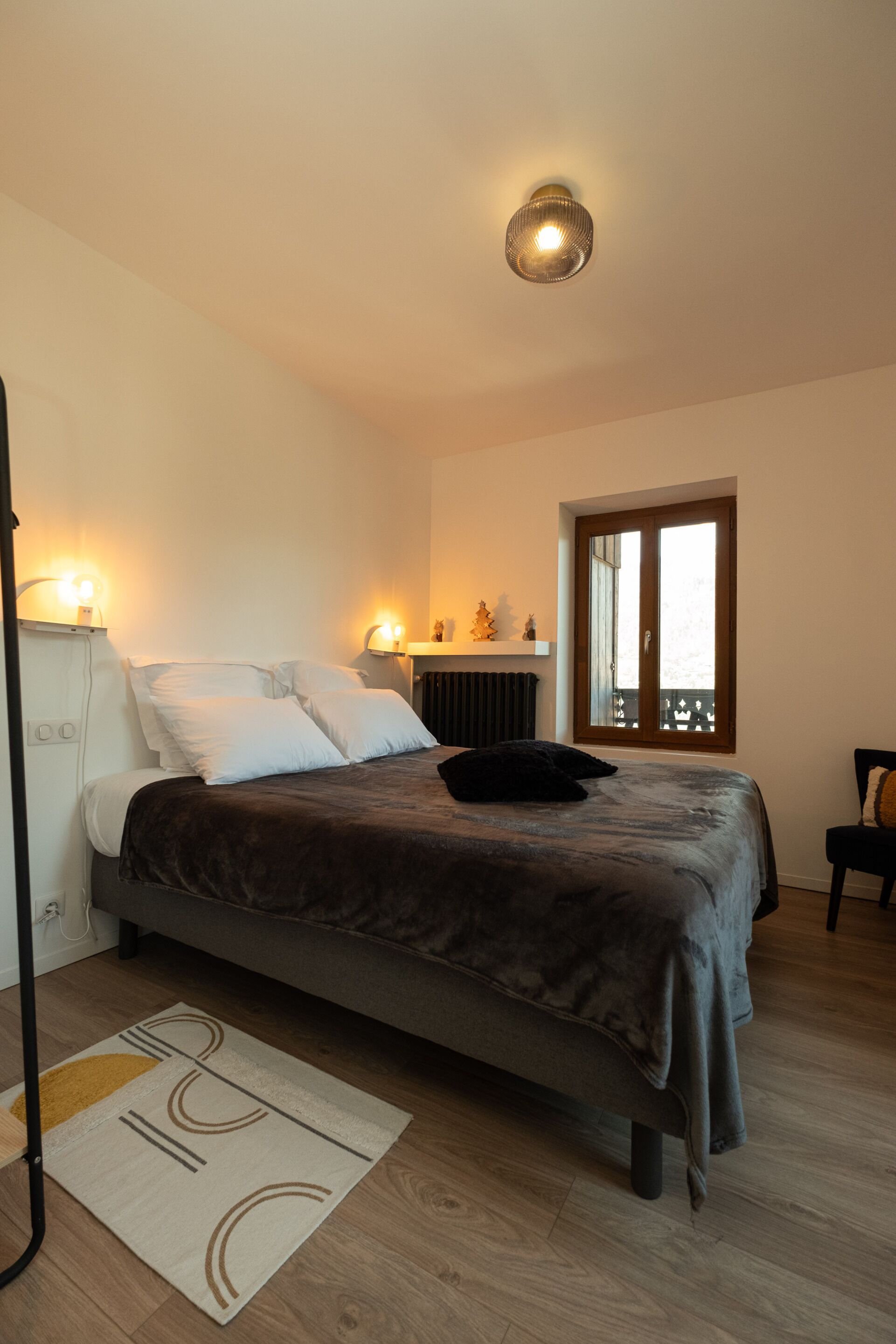 A bedroom with a bed, bedside lamps, a radiator, a window, and a chair.