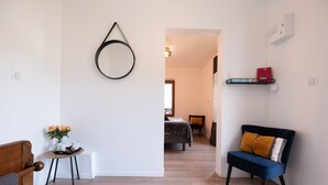 A modern living room with a round mirror, a small table with flowers, a blue sofa, and a bed in the background. - Chalet les Myrtilles (Venthon)