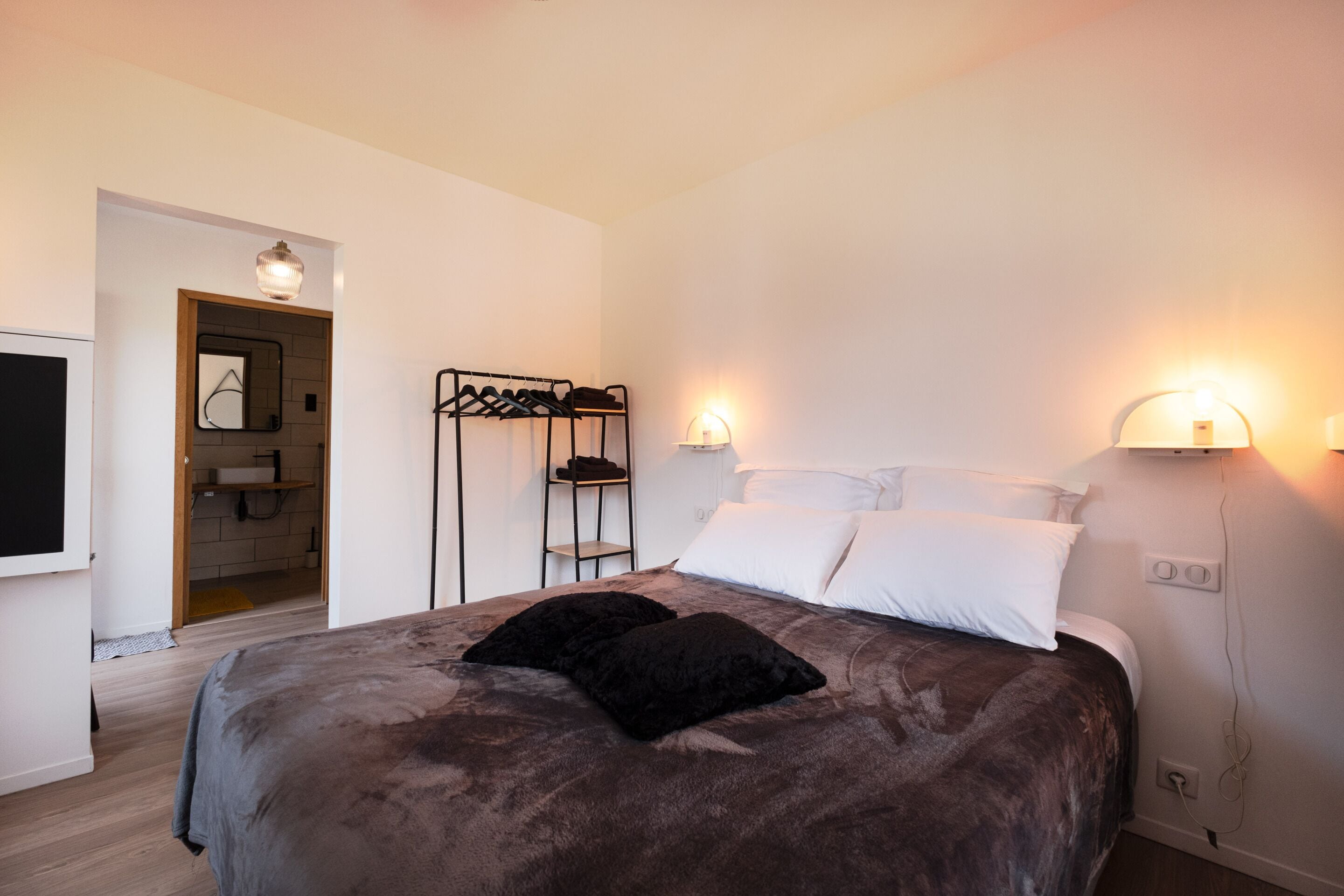 Una camera da letto con un letto, due lampade sui comodini, un appendiabiti e una porta che dà su un bagno.