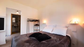 Una camera da letto con un letto, due lampade sui comodini, un appendiabiti e una porta che dà su un bagno.