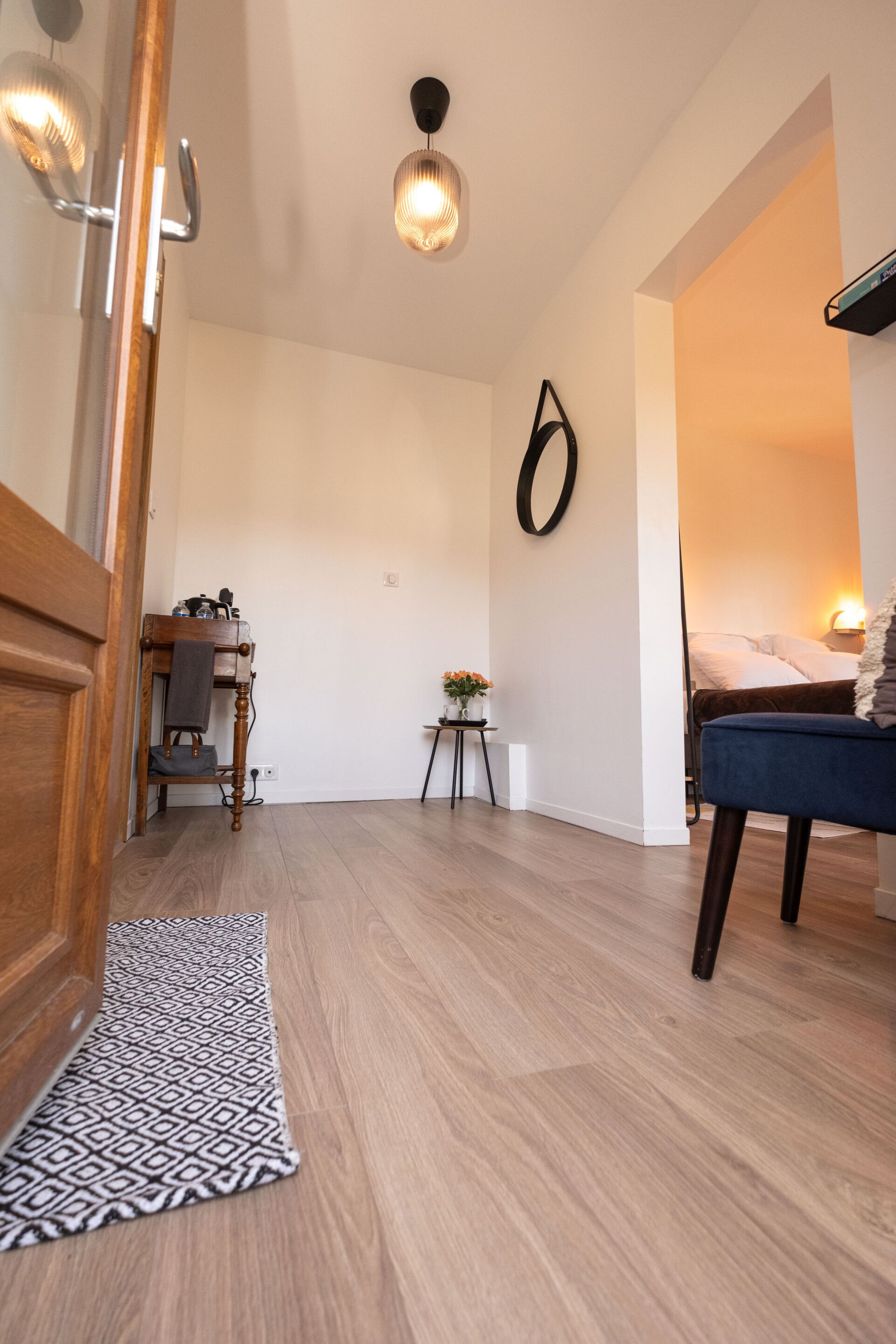 Un salon moderne avec un plancher en bois, un tapis à motifs, un canapé bleu, une petite table avec une plante et un luminaire fixé au mur.