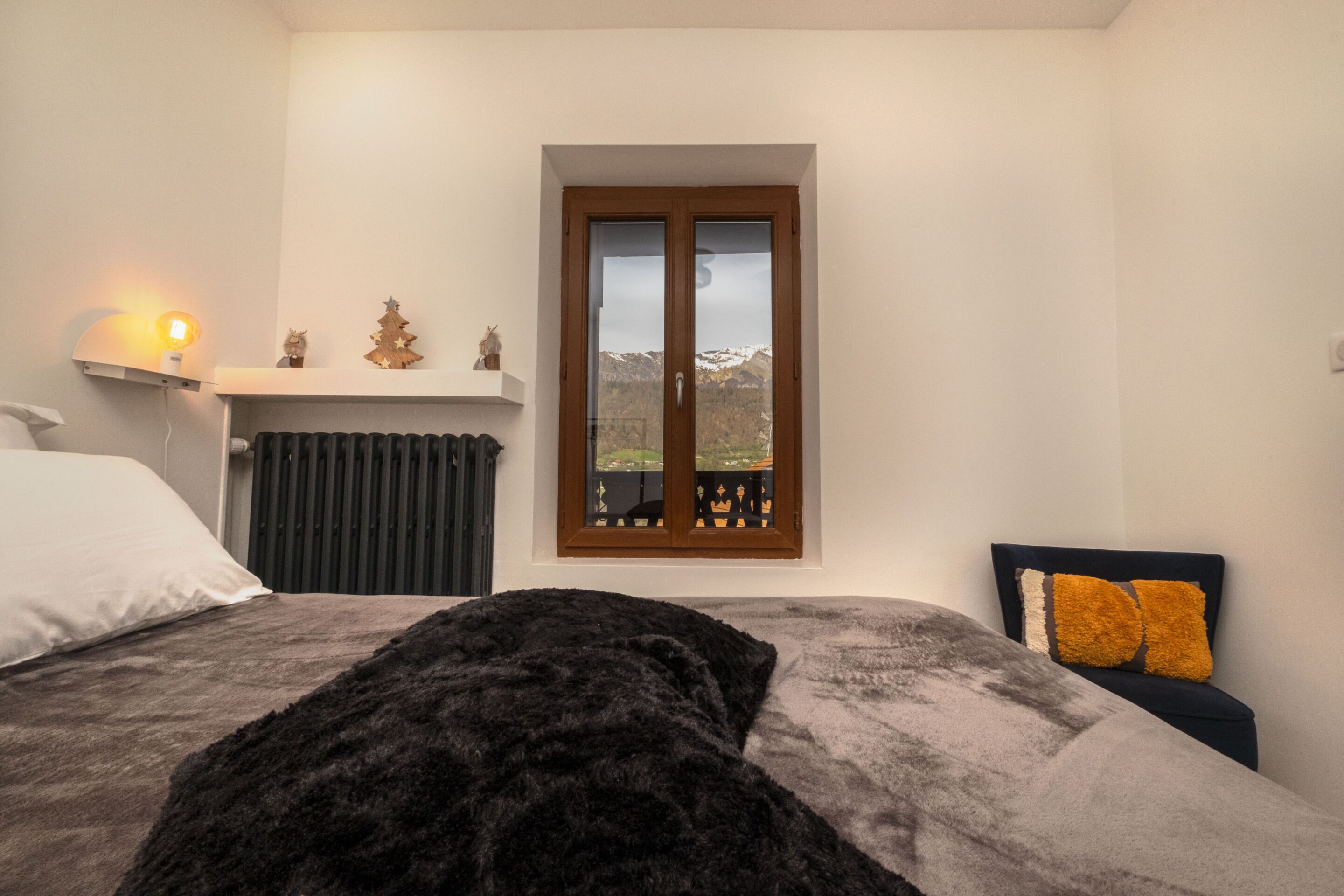 Ein Schlafzimmer mit Bett, Nachttisch, Fenster mit Blick und einer kleinen Ablage mit Dekoration.