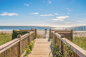 Ein hölzerner Steg führt zu einem Strand bei blauem Himmel.