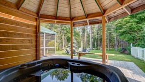 A hot tub in a wooden cabin with a glass door leading to a patio with outdoor furniture.