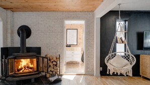A cozy living room with a wood-burning stove, a hanging chair, and a view into another room.