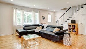 A living room with a black leather sofa, a glass coffee table, wooden flooring, a staircase, and a wooden cabinet.