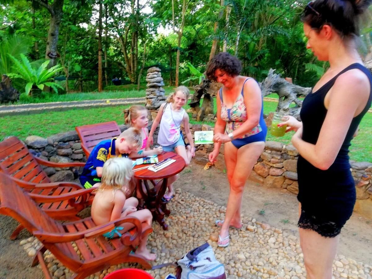 Un grupo de personas sentadas en una mesa de madera al aire libre, con un muro de piedra y follaje de fondo.