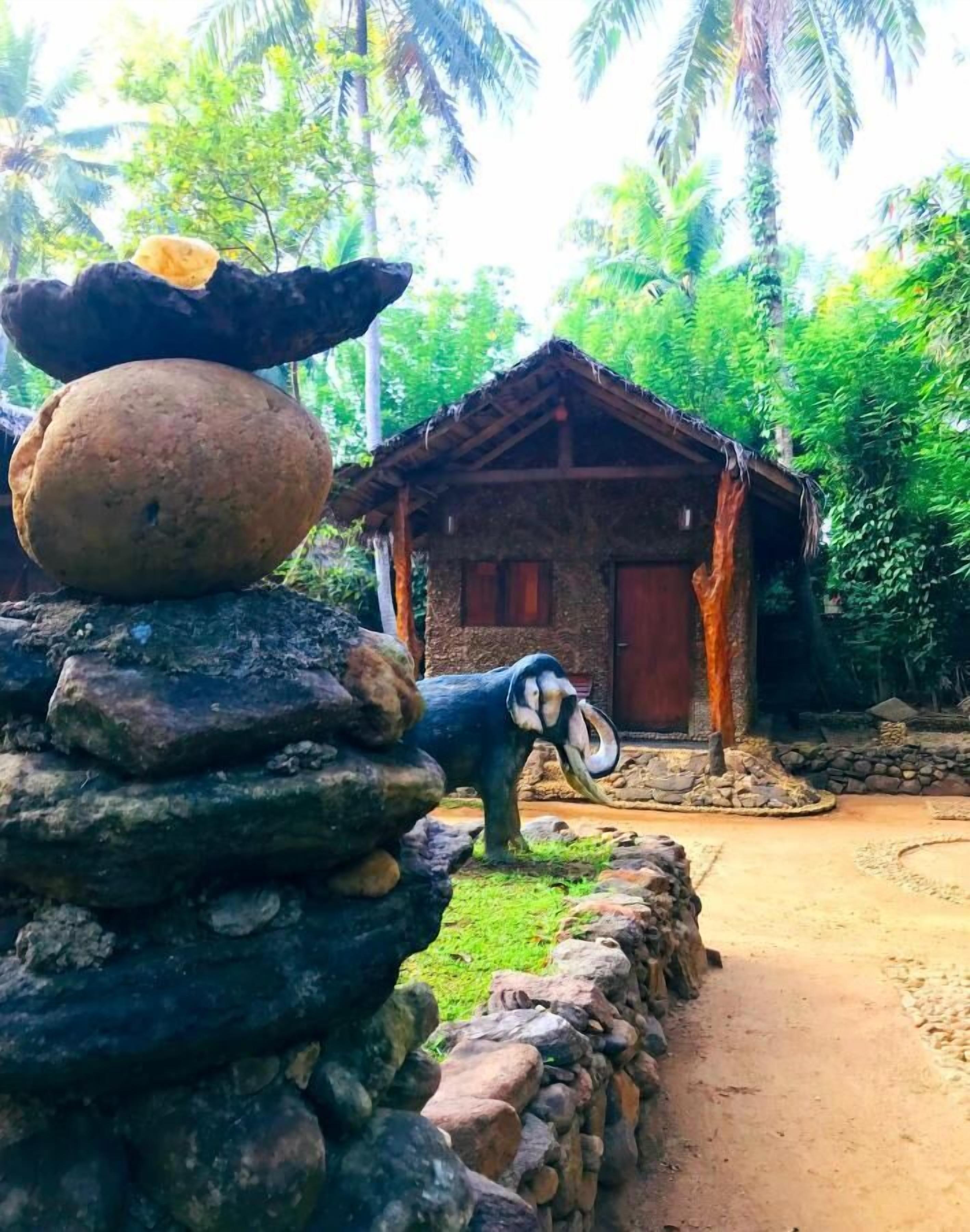 Una construcción rústica de piedra con techo de paja, rodeada de exuberante vegetación y palmeras.