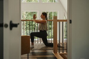 A person performing a yoga pose in a room with large windows and a wooden railing. - Kartalla - Aframe chalet lake access near Tremblant (Amherst)