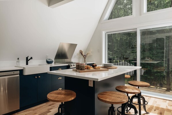 A modern kitchen with a central island, bar stools, and a large window offering a view of the outdoors.